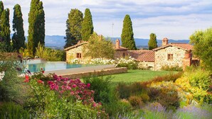 A stone house with a swimming pool, surrounded by a garden with various plants and flowers.