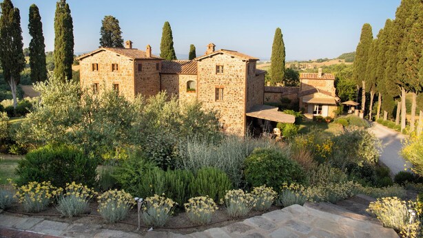 A stone building with multiple rooms, surrounded by a garden with various plants and trees.