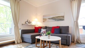 Un salon moderne avec un canapé gris, des coussins rouges et bleus, une table basse ronde en bois et un tableau accroché au mur.