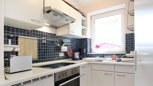 Une cuisine de taille réduite avec des meubles blancs, une cuisinière noire et une fenêtre donnant sur une fleur rose.