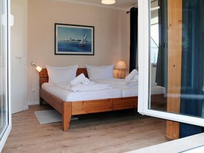 Een slaapkamer met een houten bed, wit beddengoed, een schilderij van een zeilboot en een glazen deur die uitkomt op een balkon.