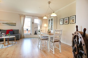 Een woonkamer met een bank, een salontafel, een eettafel met stoelen en uitzicht door een raam.