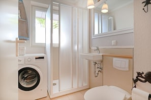 Een kleine badkamer met een wasmachine, douchecabine, wastafel en toilet.