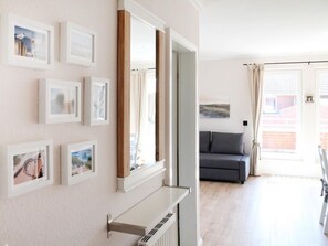 Une pièce avec un radiateur, des tableaux encadrés accrochés au mur, un canapé gris et une fenêtre avec des rideaux.