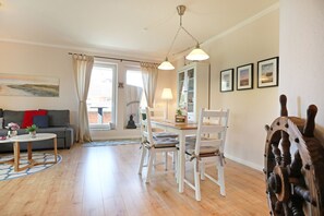 Een woonkamer met een bank, een salontafel, een eettafel met stoelen en uitzicht door een raam.