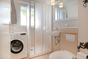 Een kleine badkamer met een wasmachine, douchecabine, wastafel en toilet.