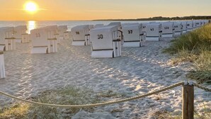 Une rangée de cabanes de plage numérotées, sur une plage de sable, avec le soleil couchant en arrière-plan.