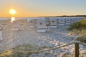 Une rangée de cabanes de plage numérotées, sur une plage de sable, avec le soleil couchant en arrière-plan.