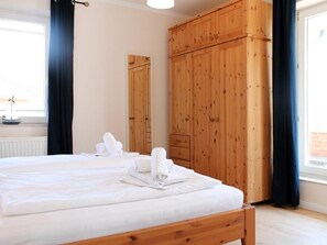 A bedroom with a wooden bed frame, a large wardrobe, and a window with curtains.