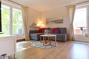 Een moderne woonkamer met een grijze bank, rode kussens, een ronde salontafel en een schilderij aan de muur.