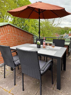 Un patio al aire libre con una mesa, sillas, un paraguas rojo y una botella de vino.