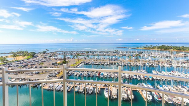 Un puerto deportivo con numerosos barcos amarrados, cielo despejado y vista al océano.