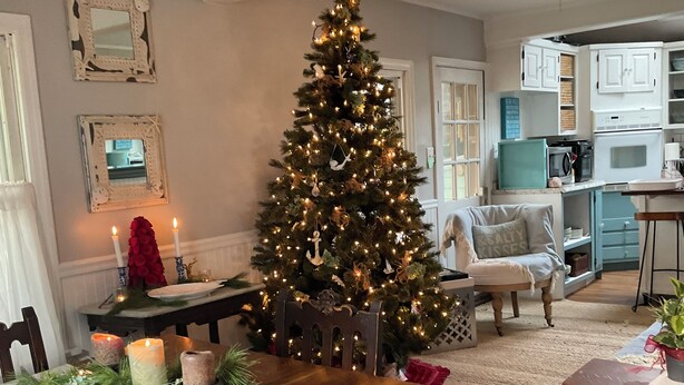 A cozy dining area with a Christmas tree, candles, and a table set for a meal.