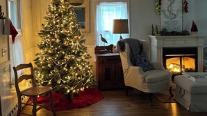 A cozy living room with a lit Christmas tree, a fireplace, and a comfortable armchair.