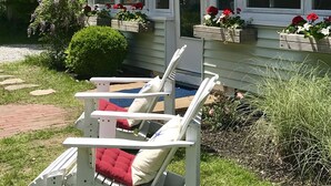 A white house with a covered porch, a lawn chair with red cushions, and flower boxes on the windowsills.
