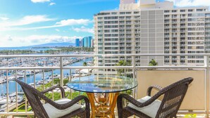 A balcony with wicker chairs and a glass table overlooking a marina and cityscape. - Beautiful Marina Sunset Views, Located In The Ilikai Hotel! (Honolulu)