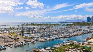 A marina with numerous boats docked, surrounded by greenery and palm trees, with a clear sky above. - Beautiful Marina Sunset Views, Located In The Ilikai Hotel! (Honolulu)