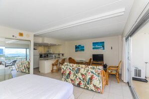 A hotel room with a bed, a dining area with chairs, a kitchen, and a balcony with a view.