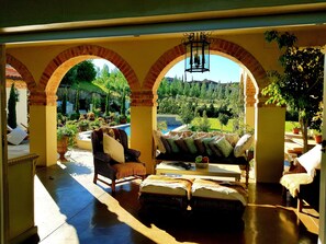 A sunlit room with a view of a garden and pool, featuring a sofa, armchairs, and a table. - Sandmartins (Paarl)
