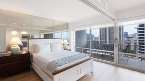 Un dormitorio moderno con una cama grande, lámparas de noche, un tocador y un balcón con vistas a la ciudad.