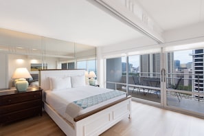 A modern bedroom with a large bed, bedside lamps, a dresser, and a balcony with a city view.