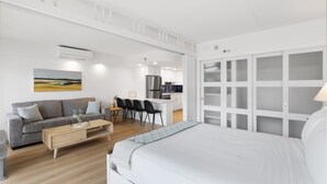 Una habitación de hotel moderna con cama, sofá, comedor y cocina al fondo.