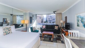 A hotel room with a bed, a sofa, a coffee table, a TV, and a balcony with a city view.