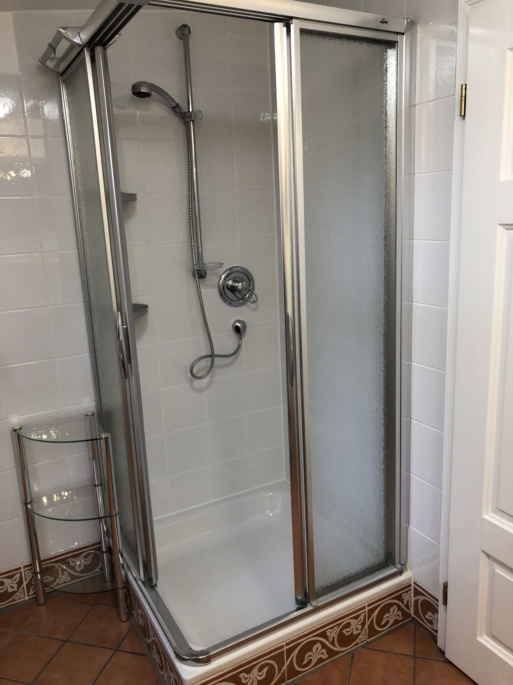 A glass-enclosed shower with a chrome frame, a glass shelf, and a tiled floor.