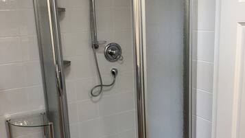 A glass-enclosed shower with a chrome frame, a glass shelf, and a tiled floor.