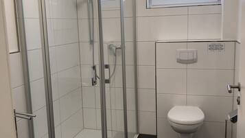 Un bagno moderno con doccia vetrata, un water e una finestra sopra il lavabo.