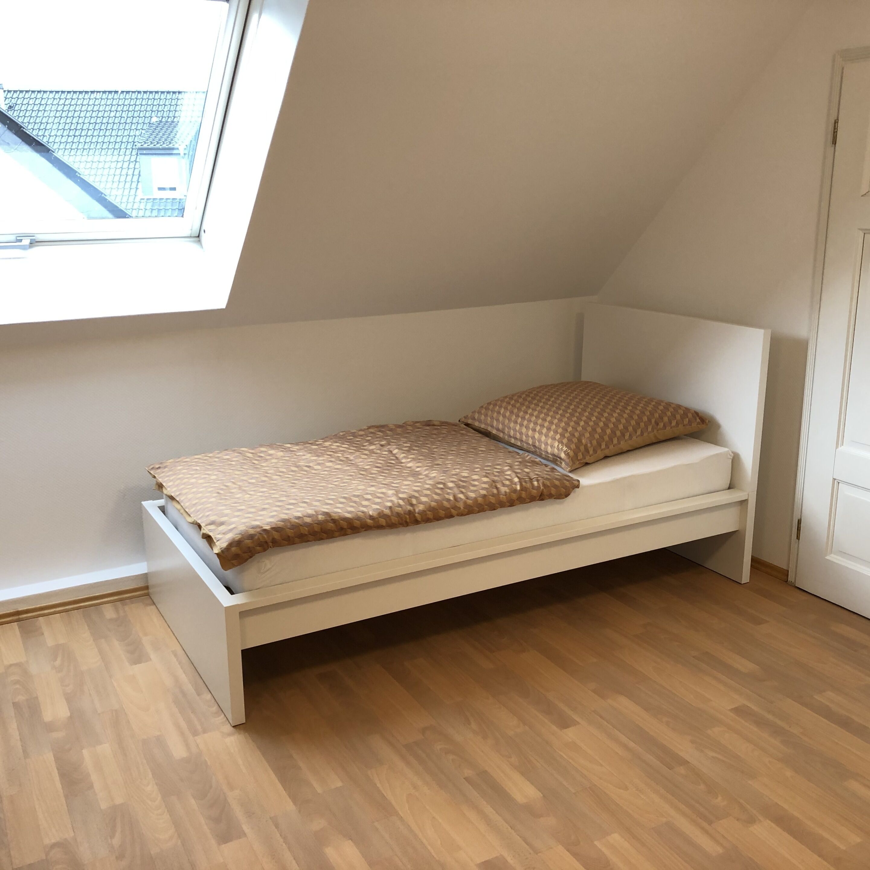 A small, single-bed room with a sloped ceiling and a window.