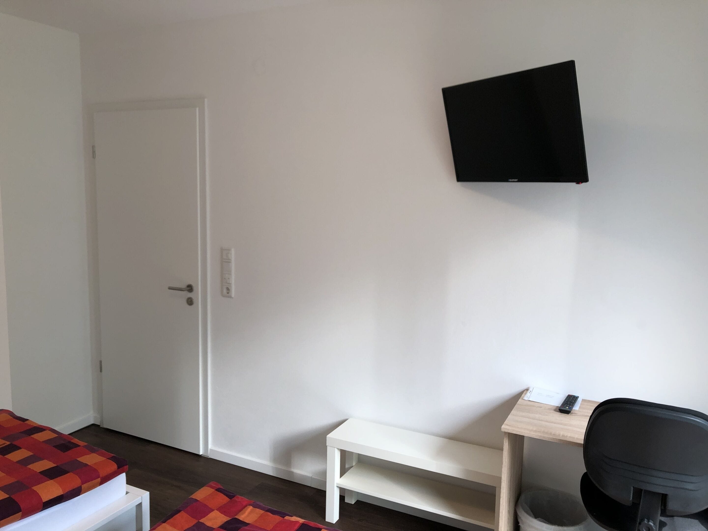 Une chambre avec un lit, un bureau, une chaise et un téléviseur fixé au mur.