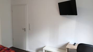 Une chambre avec un lit, un bureau, une chaise et un téléviseur fixé au mur.