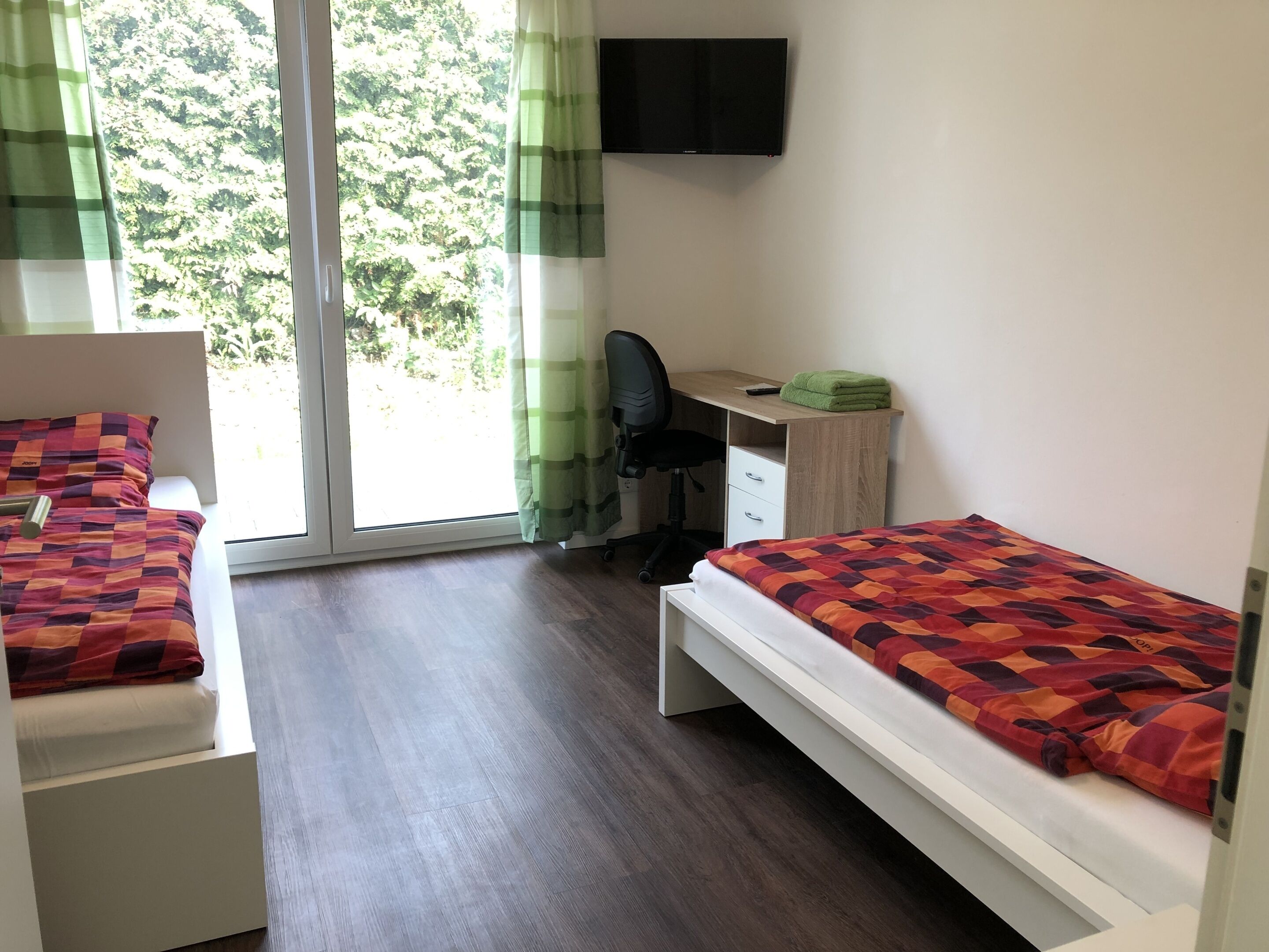 A room with two beds, a desk, a chair, and a TV.