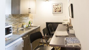 A compact kitchen with a microwave, sink, and a small refrigerator. There is a dining table with chairs and a radiator above it. - Pair of studio apartments in the Langhe with swimming pool, panoramic terrace and green area (Cossano Belbo)