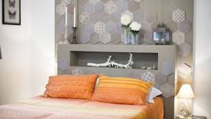 A bedroom with a bed, decorative wall tiles, a shelf with items, and a framed picture. - Pair of studio apartments in the Langhe with swimming pool, panoramic terrace and green area (Cossano Belbo)