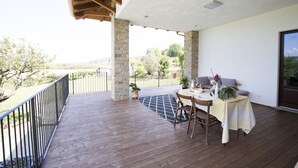 A covered outdoor area with a wooden deck, a table with chairs, and a view of the surrounding landscape. - Pair of studio apartments in the Langhe with swimming pool, panoramic terrace and green area (Cossano Belbo)