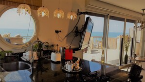 Een keuken met uitzicht op zee, een rond raam en een eethoek met een tafel en stoelen.