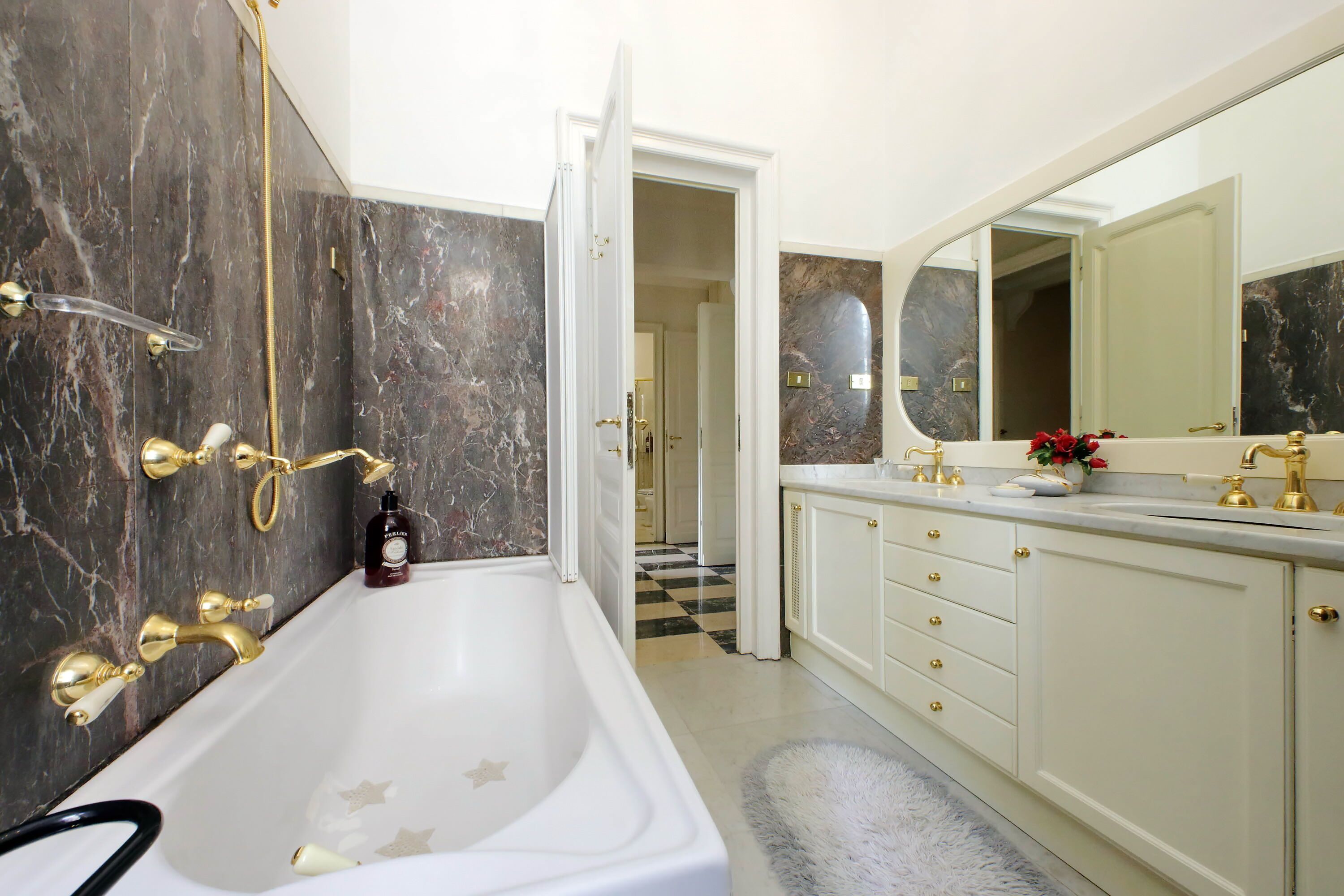 A bathroom with a large bathtub, marble walls, and a vanity with a mirror.