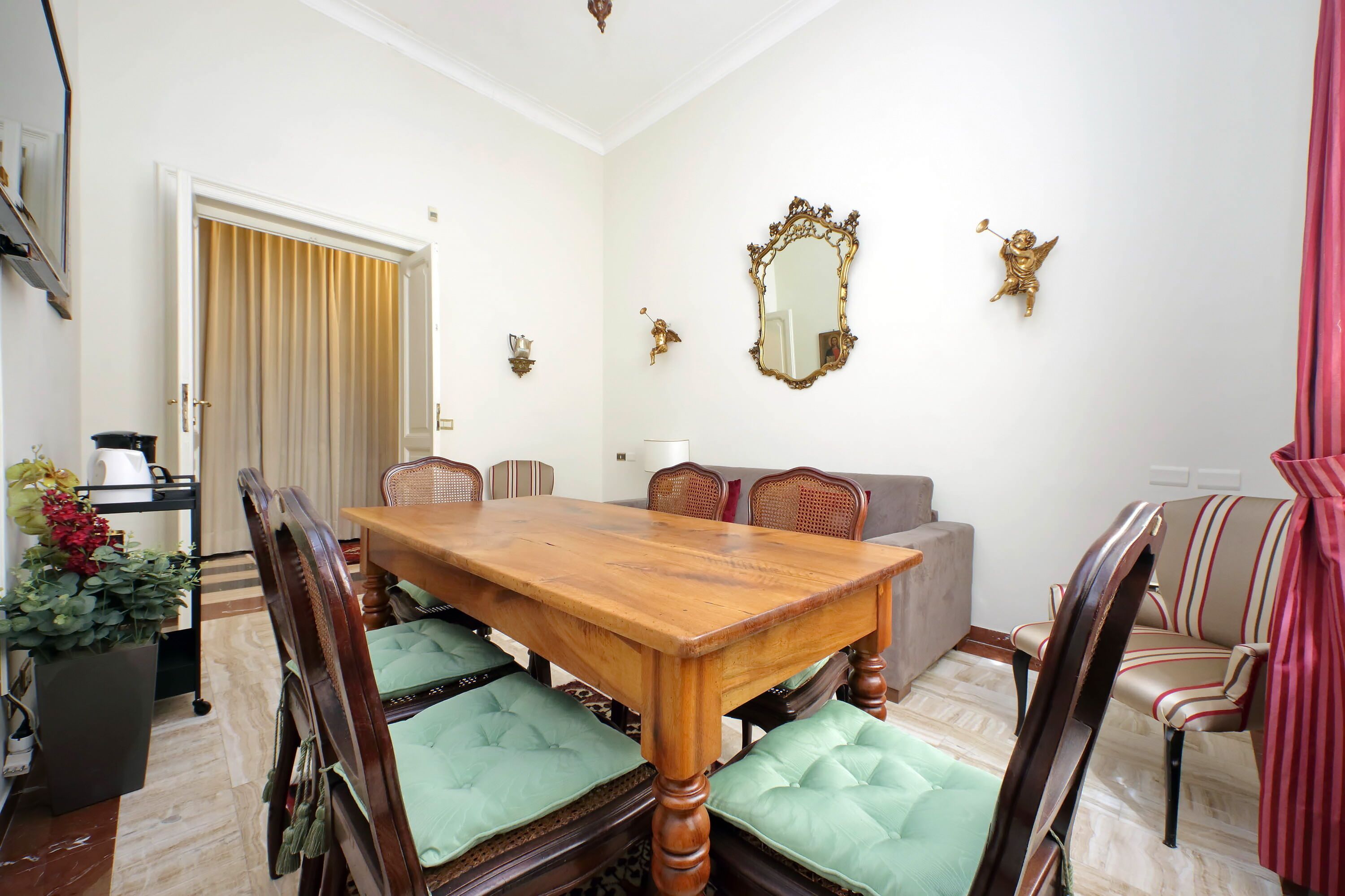 A dining room with a wooden table and chairs, a sofa, and a mirror on the wall.