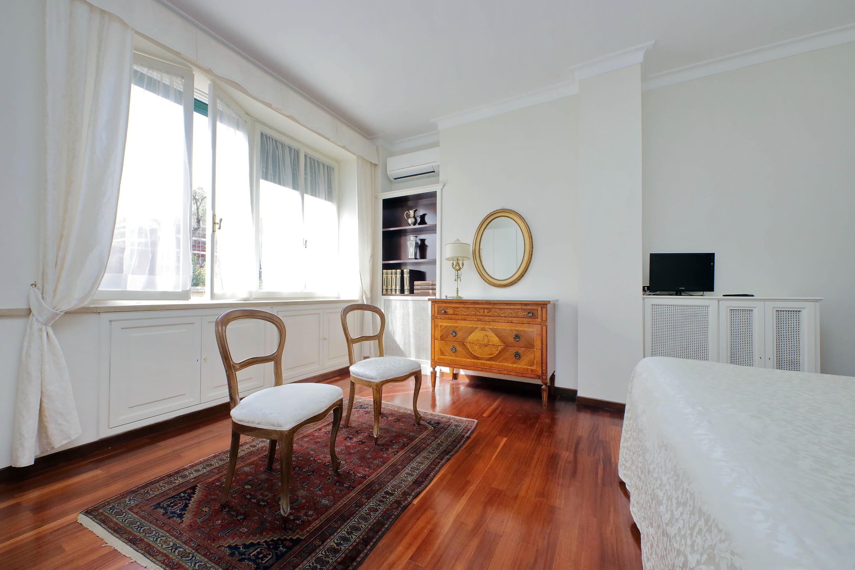 A bedroom with a wooden dresser, a mirror, a television, and a bed.