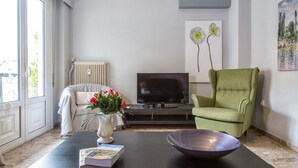 A living room with a sofa, a green armchair, a TV, a vase with flowers, and a book on a coffee table. - Margarita's home cozy home! (Athina)