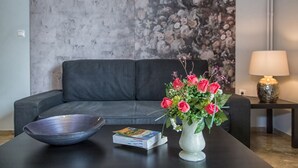 A modern living room with a grey sofa, a coffee table with a bowl and a book, and a vase with flowers. - Margarita's home cozy home! (Athina)