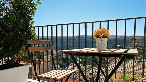 A balcony with a wooden table and chairs, a potted plant, and a view of a distant landscape. - ChocoHouse (Ragusa)