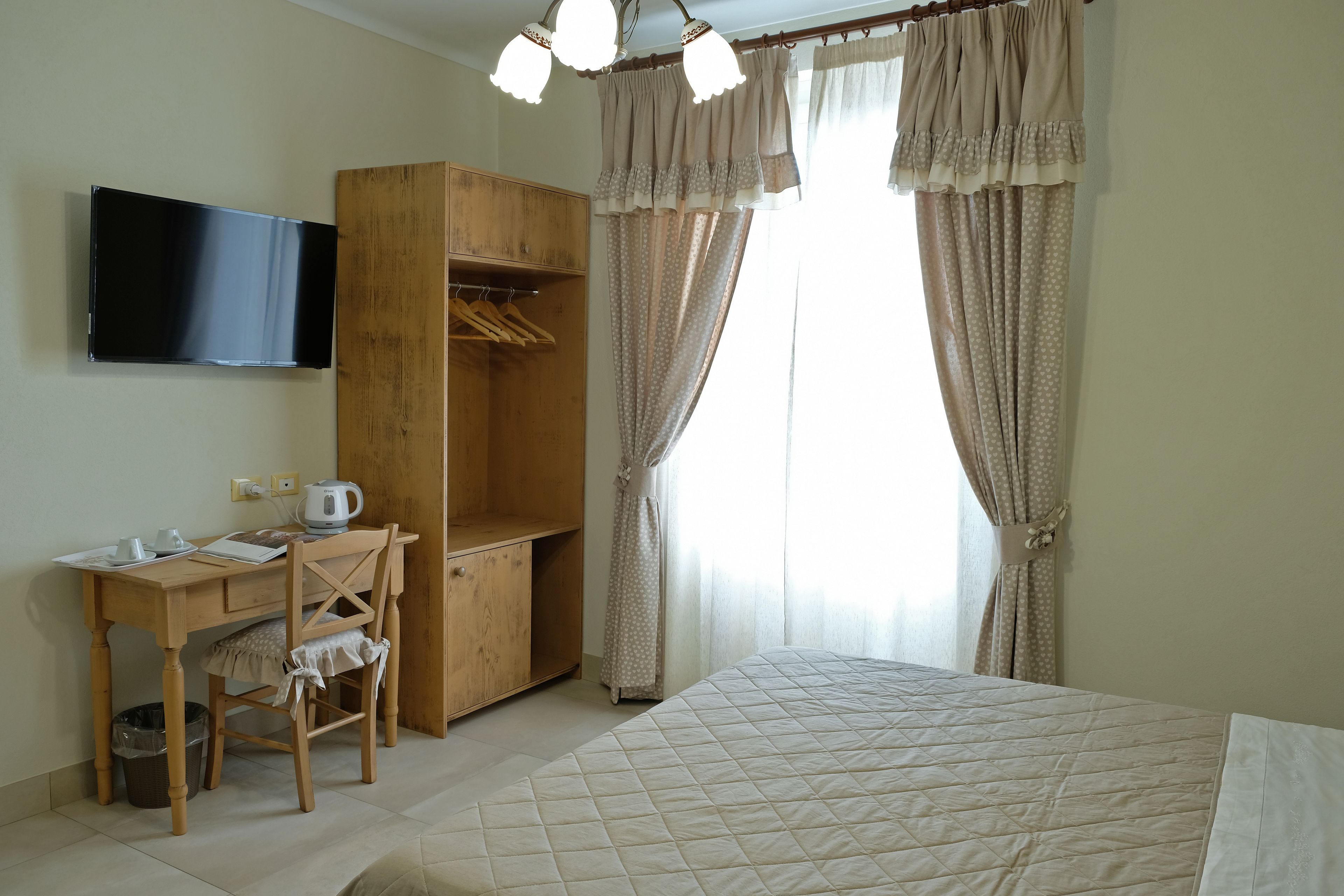 A bedroom with a bed, a wooden desk with a chair, a TV mounted on the wall, and a wardrobe.