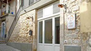 A stone building with a white door and a sign indicating it houses a chocolate house, cafe, rooms, and a factory. - ChocoHouse (Ragusa)