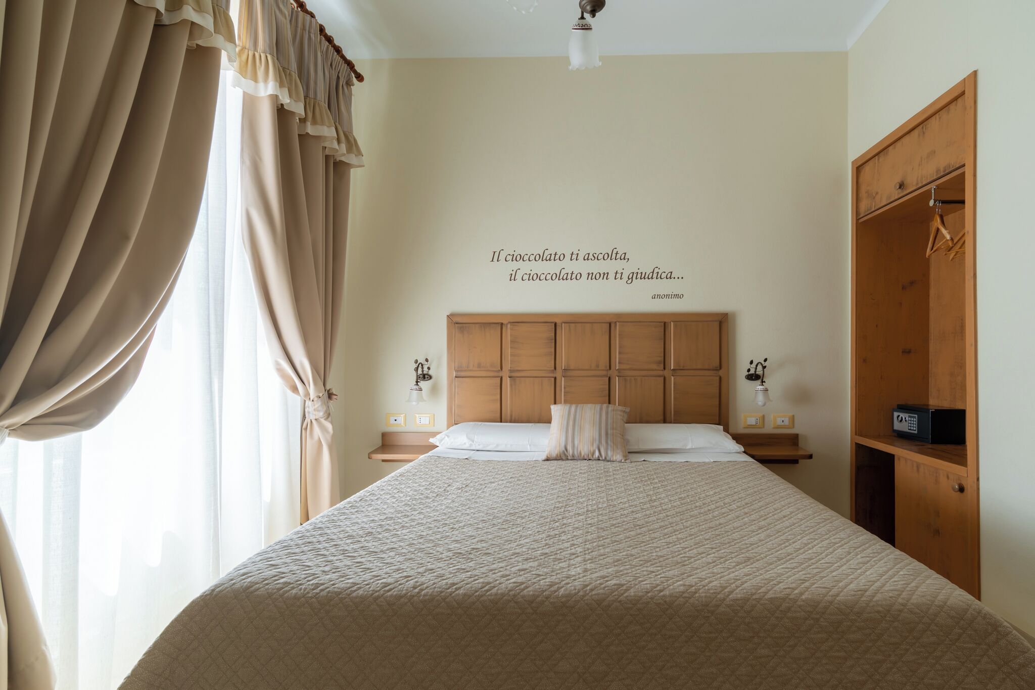 Une chambre à coucher avec un grand lit, une tête de lit en bois, des tables de chevet avec des lampes, une armoire et un mur orné d’une citation.