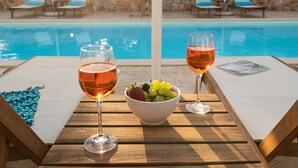 Taula al costat de la piscina amb dues copes de vi rosat, un plat de fruita i una revista.