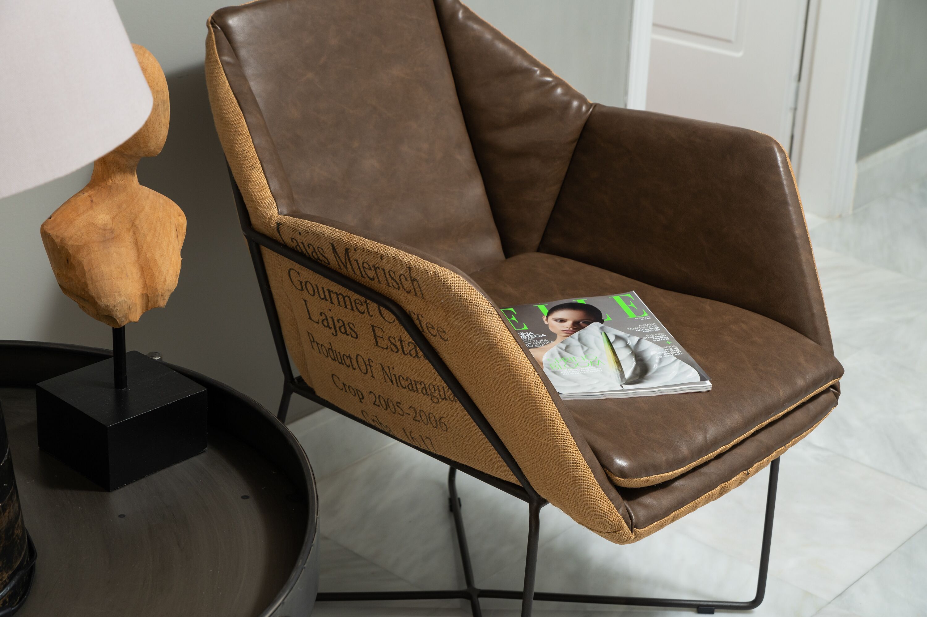 Un fauteuil en cuir marron, sur lequel repose un magazine, est placé à côté d’une sculpture en bois posée sur un socle noir.