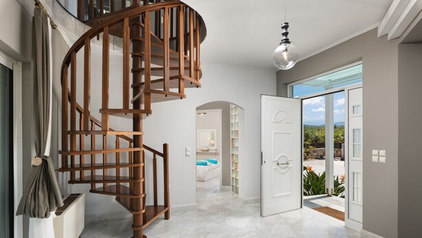 Un interior espaiós amb una escala espiraltra, una gran porta de vidre que dona a l'exterior i vista a un jardí.